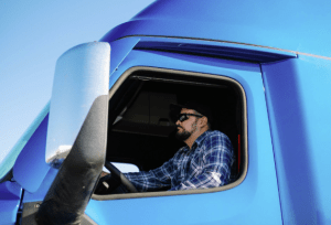 Chauffeur de camion lourd francophone devant son véhicule sur une route d'Ontario.